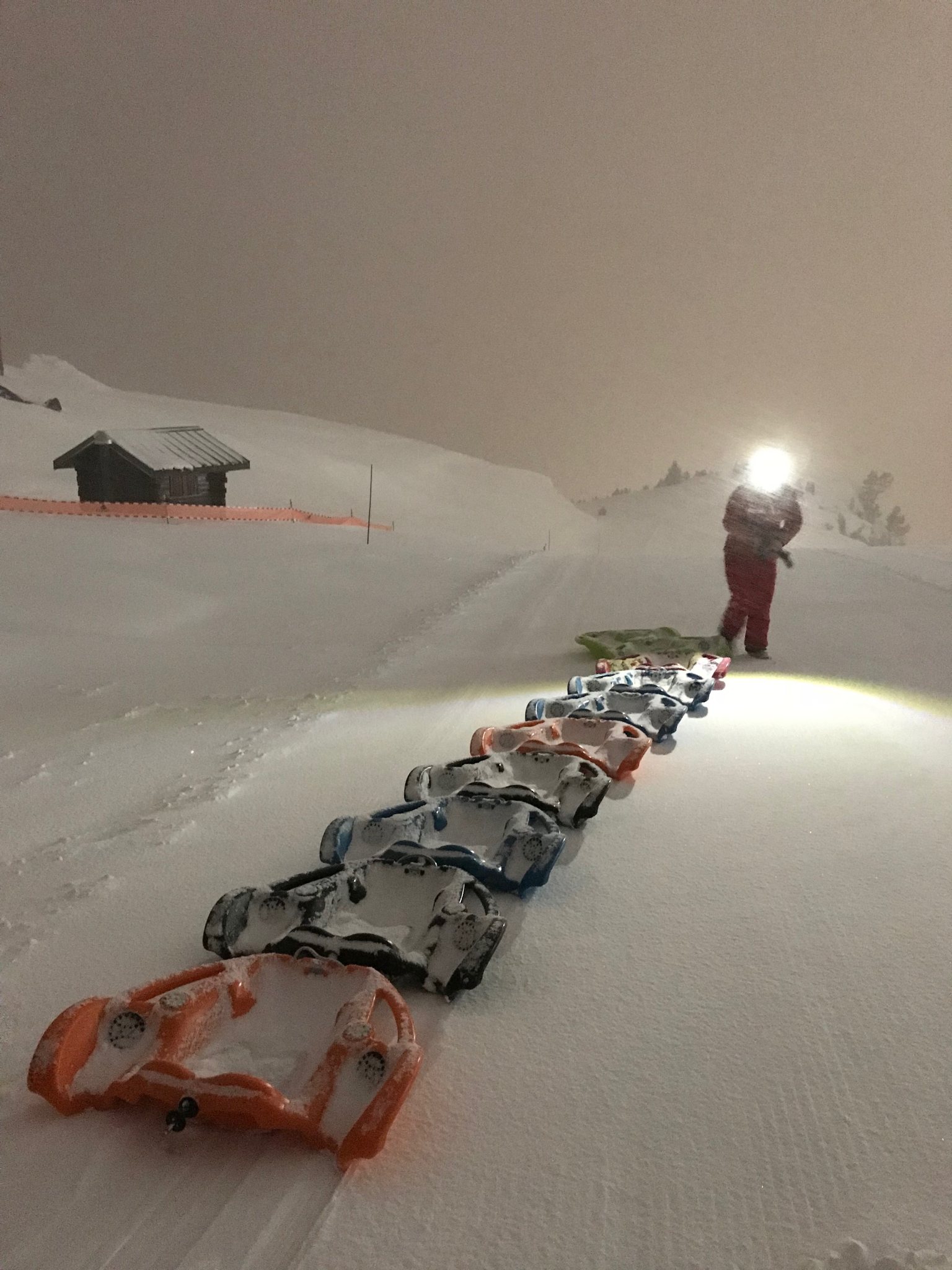 Plusieurs snowboards sont alignés sur la piste de nuit, avec une lumière au loin