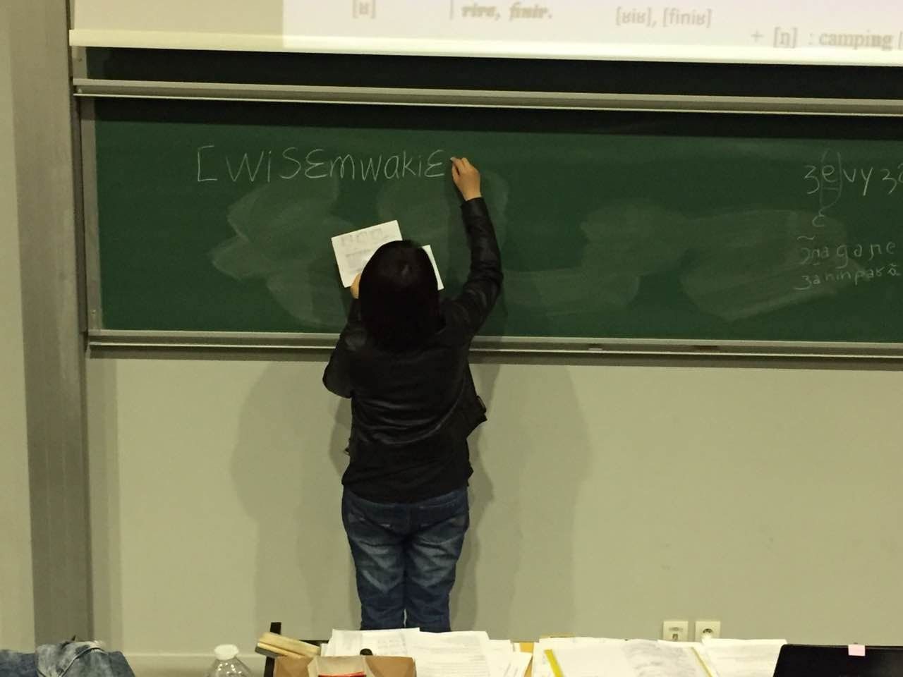 Une personne écrit au tableau tandis que des documents sont étalés sur les tables